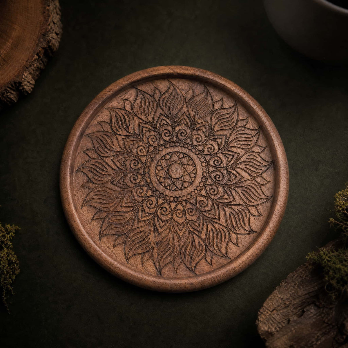 Hand-carved walnut coaster with floral mandala pattern, top view on dark background